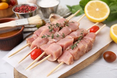 Photo of Skewers with cut raw meat, thyme and tomatoes on light table, closeup