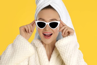 Beautiful young woman in bathrobe and sunglasses on yellow background