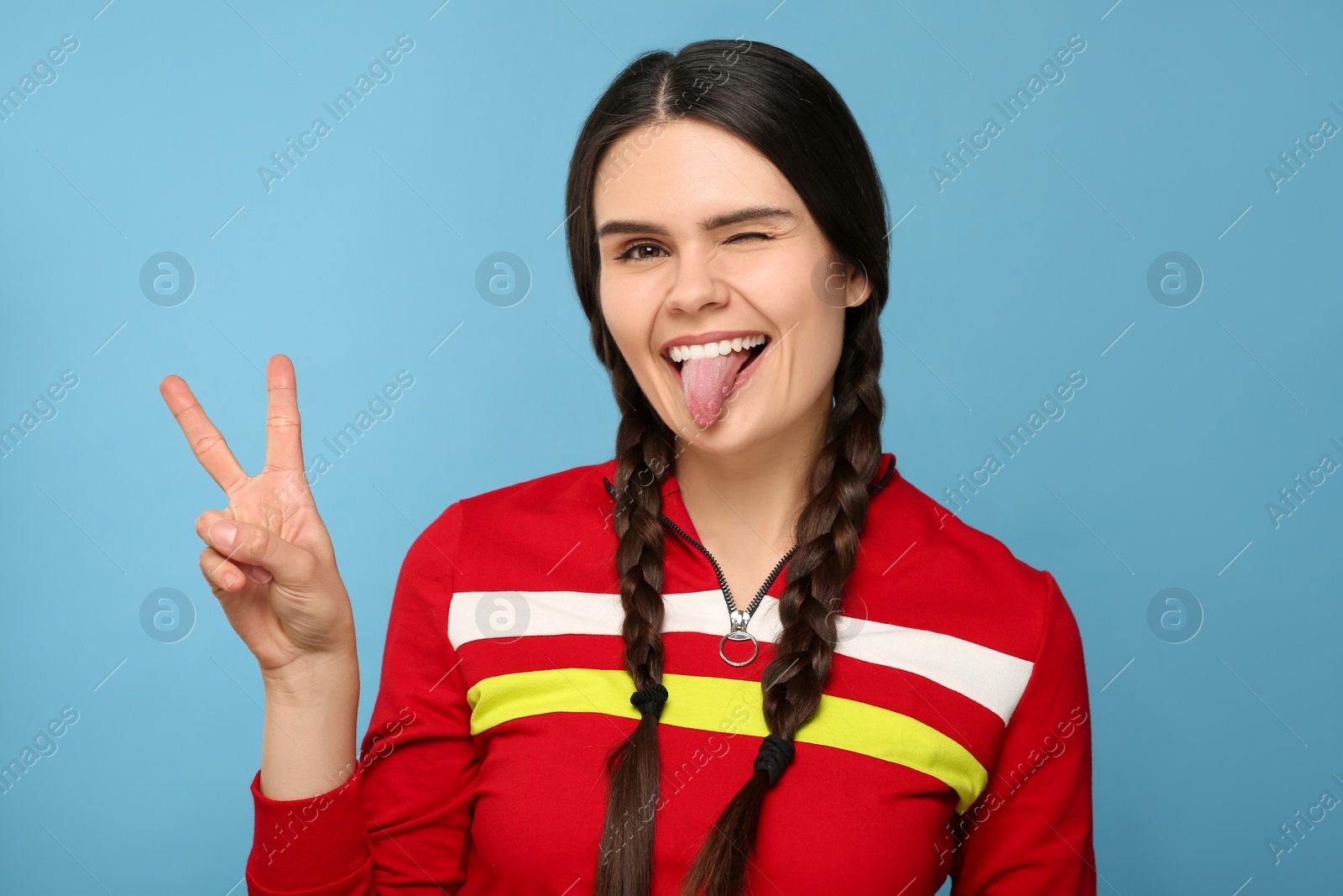 Photo of Happy young woman showing her tongue on light blue background