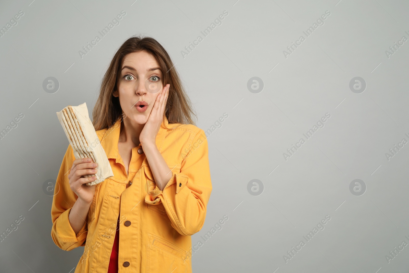 Photo of Emotional young woman with delicious shawarma on grey background, space for text