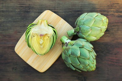 Whole and cut fresh raw artichokes on wooden table, flat lay