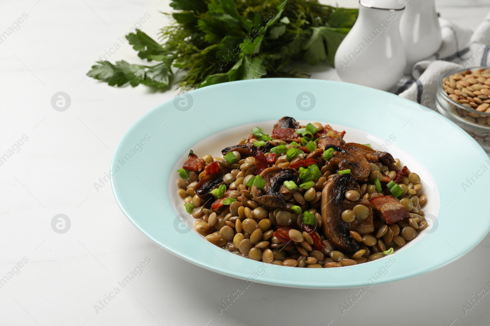 Photo of Delicious lentils with mushrooms, bacon and green onion on white table, closeup