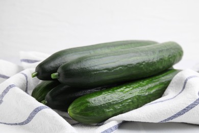 Photo of Fresh cucumbers and cloth on white table, closeup