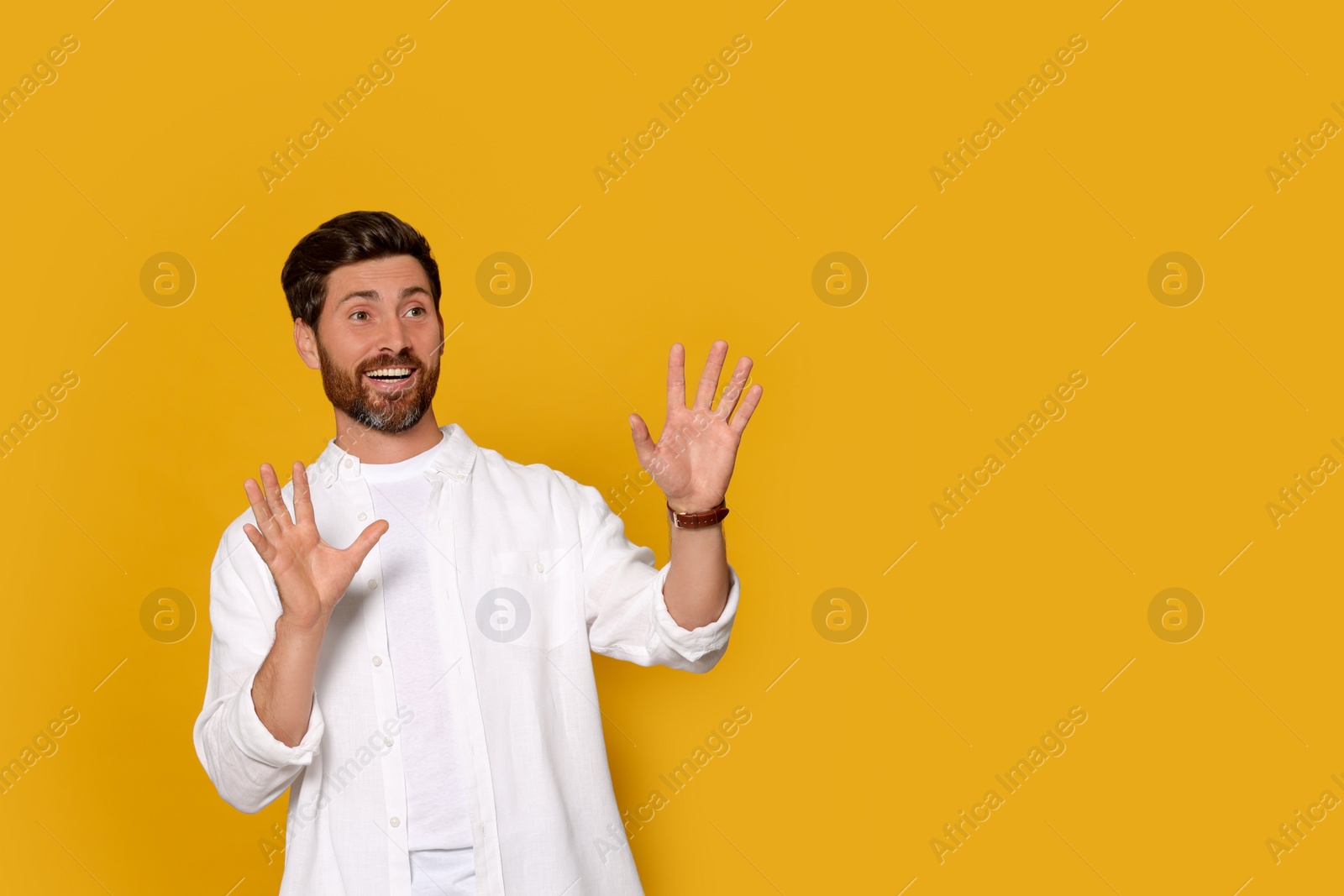 Photo of Portrait of emotional bearded man with open hands on orange background. Space for text