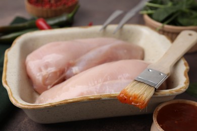 Photo of Marinade, basting brush and raw chicken fillets on brown table, closeup