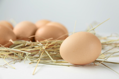 Photo of Raw chicken egg and decorative straw on white table, closeup