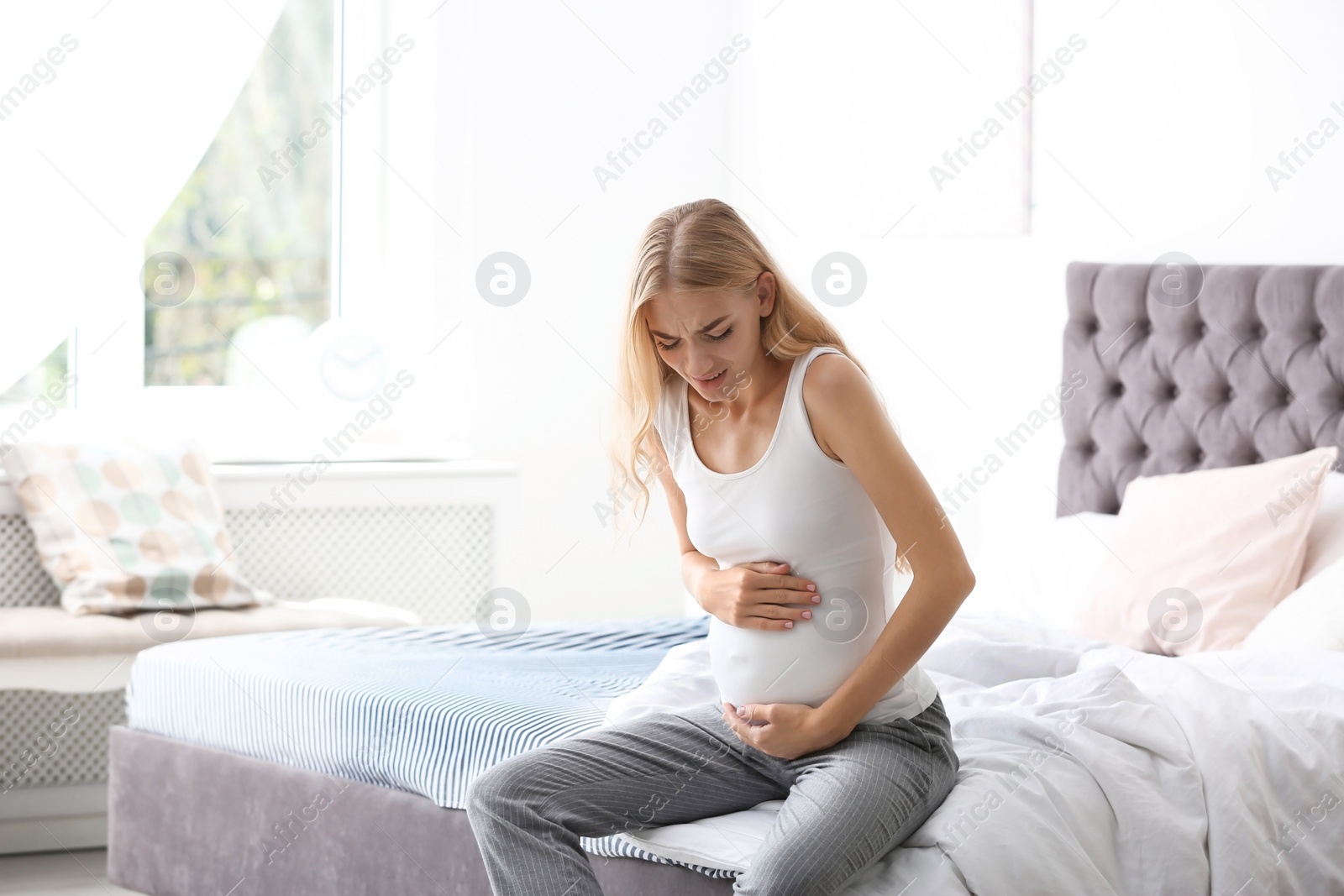 Photo of Young pregnant woman suffering from pain in bedroom. Gynecology concept