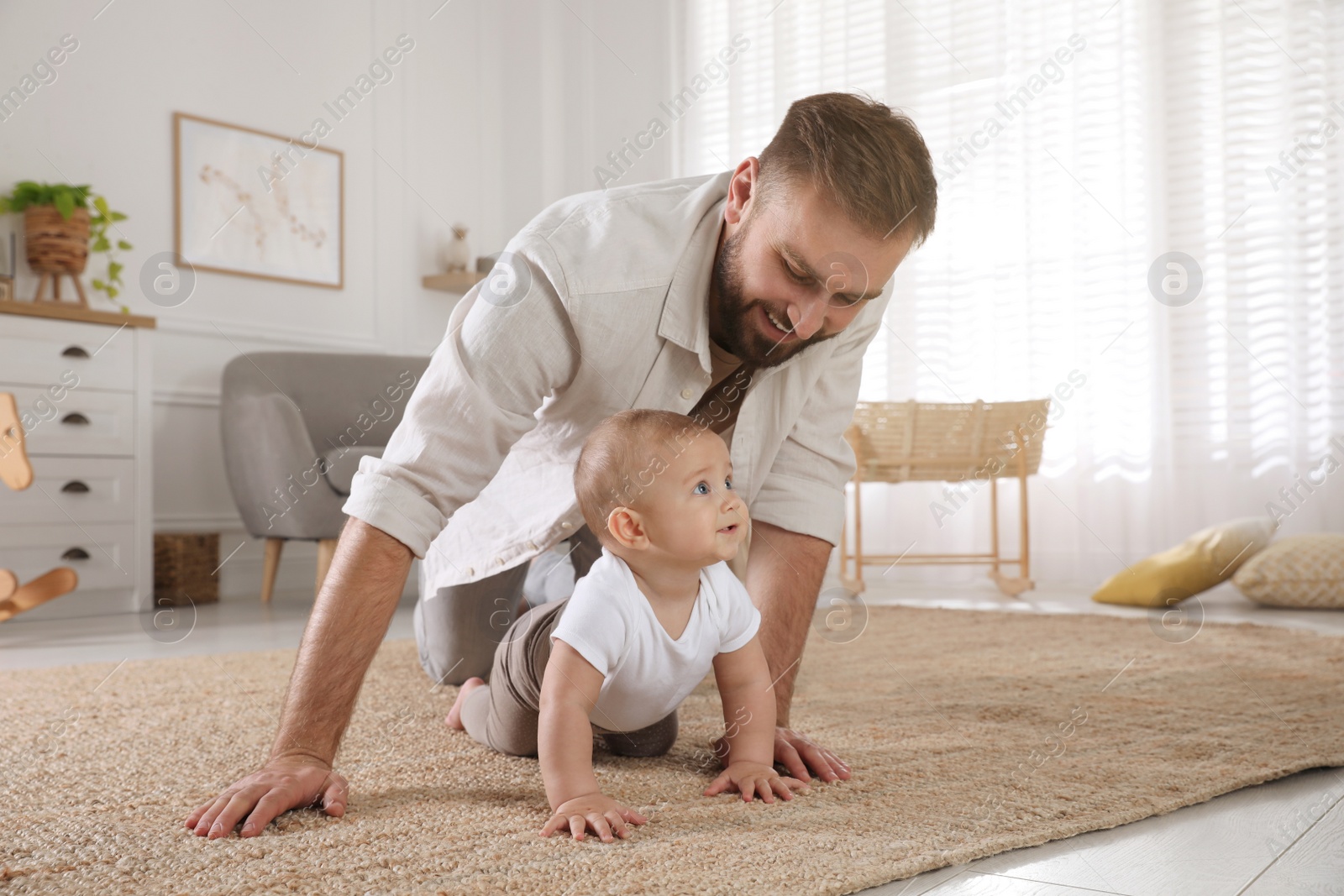 Photo of Happy young father watching his cute baby crawl on floor at home