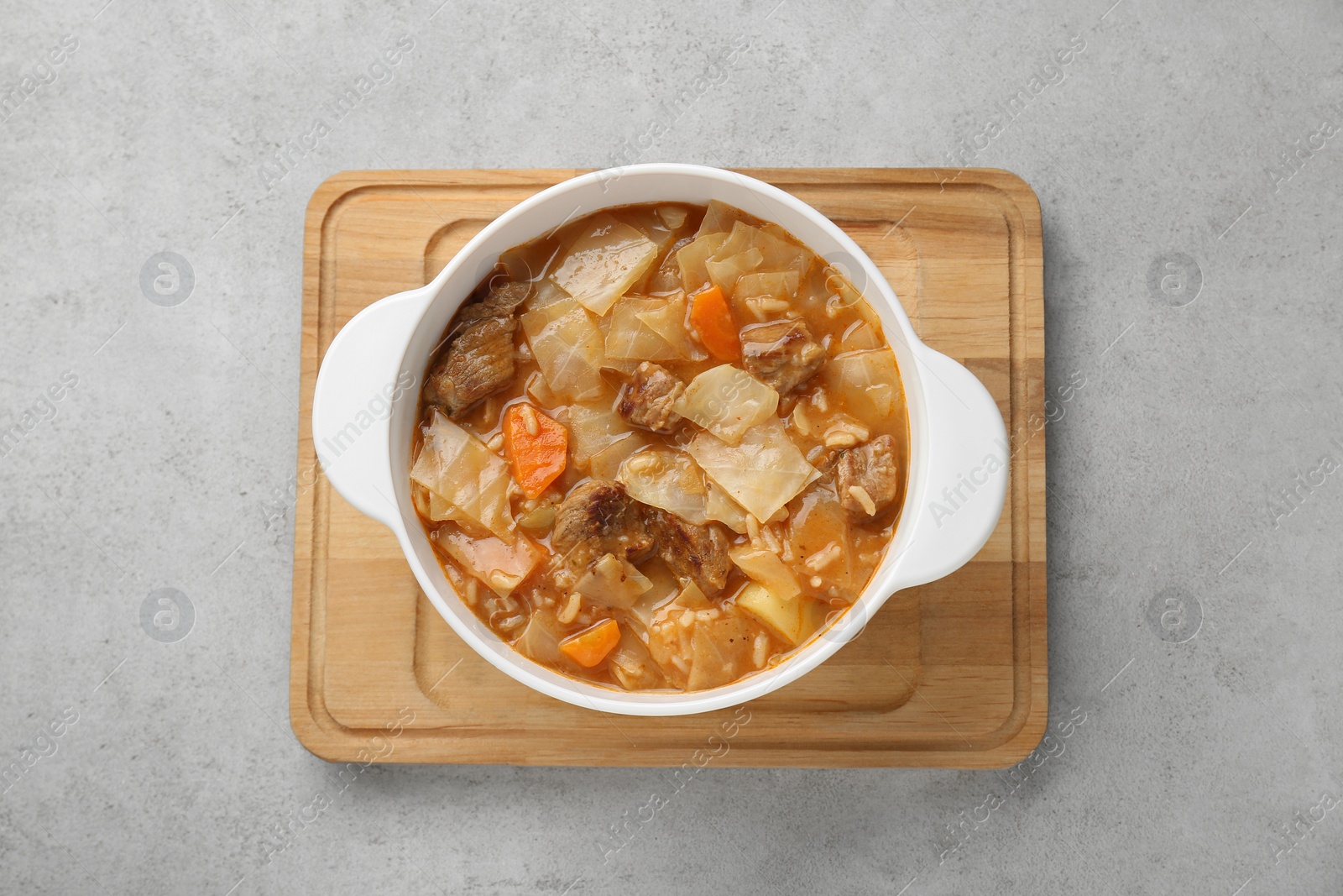 Photo of Tasty cabbage soup with meat and carrot on light grey textured table, top view