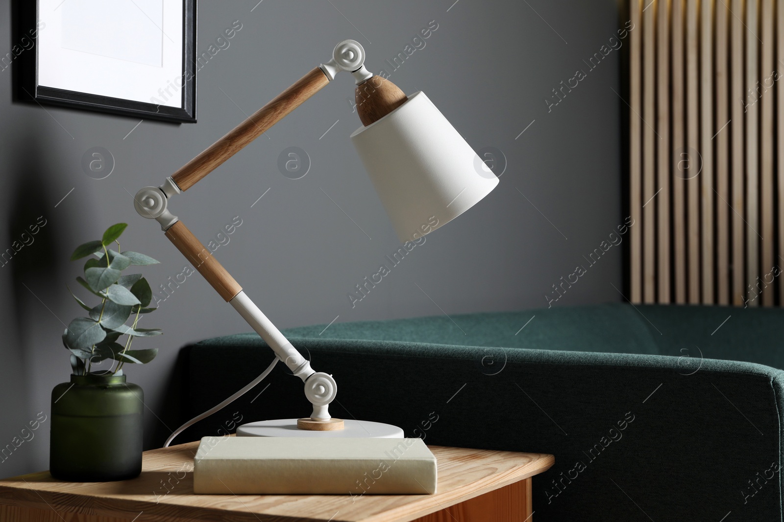 Photo of Stylish modern desk lamp, book and plant on wooden cabinet in living room