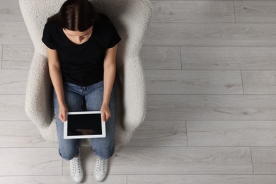 Woman working with tablet in armchair, top view. Space for text