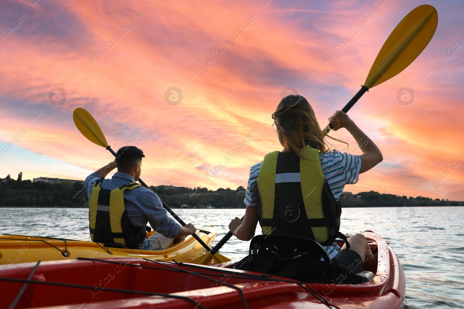 Photo of Couple in life jackets kayaking on river, back view. Summer activity