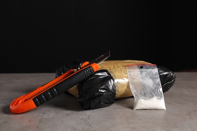 Photo of Smuggling, drug trafficking. Packages with narcotics and utility knife on grey table against black background