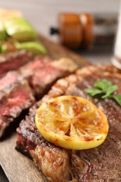 Photo of Delicious grilled beef steak and lemon slice on table, closeup