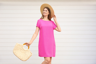 Beautiful young woman with stylish straw bag near white wall