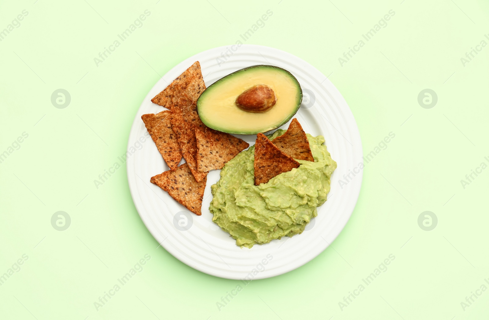 Photo of Delicious guacamole, avocado and nachos on light green background, top view