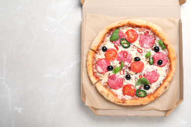 Photo of Delicious pizza Diablo in cardboard box on light marble background, top view. Space for text