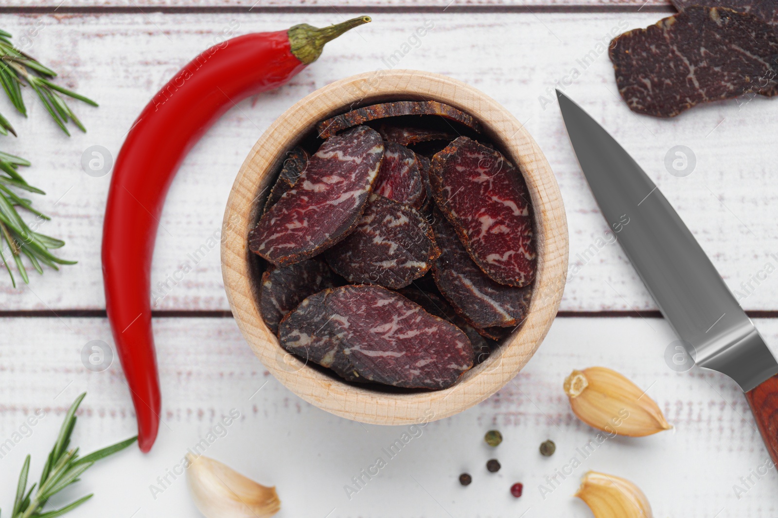 Photo of Slices of delicious beef jerky and ingredients on white wooden table, flat lay