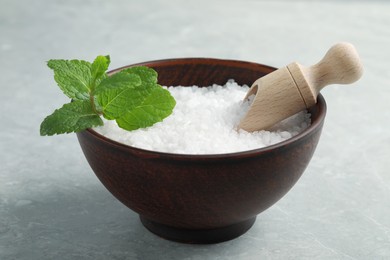 Photo of Natural sea salt in wooden bowl, scoop and mint on light grey marble table