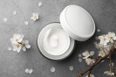 Flat lay composition with jar of face cream and flowers on grey table