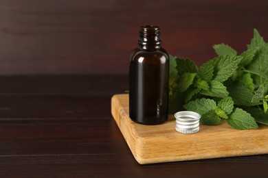 Glass bottle of nettle oil with leaves on wooden table. Space for text