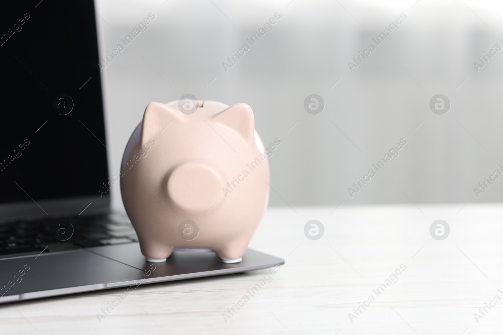 Photo of Piggy bank and laptop on white table indoors. Space for text