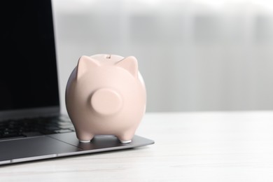 Piggy bank and laptop on white table indoors. Space for text