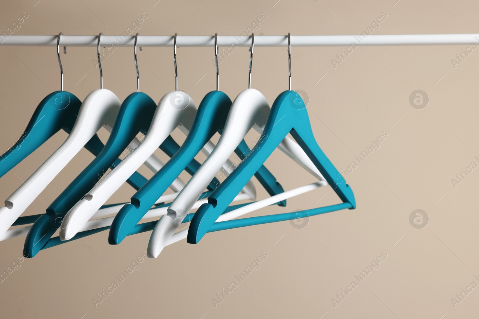 Photo of Clothes hangers on metal rail against beige background
