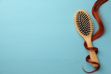 Photo of Brush and red hair strand on light blue wooden table, top view. Space for text