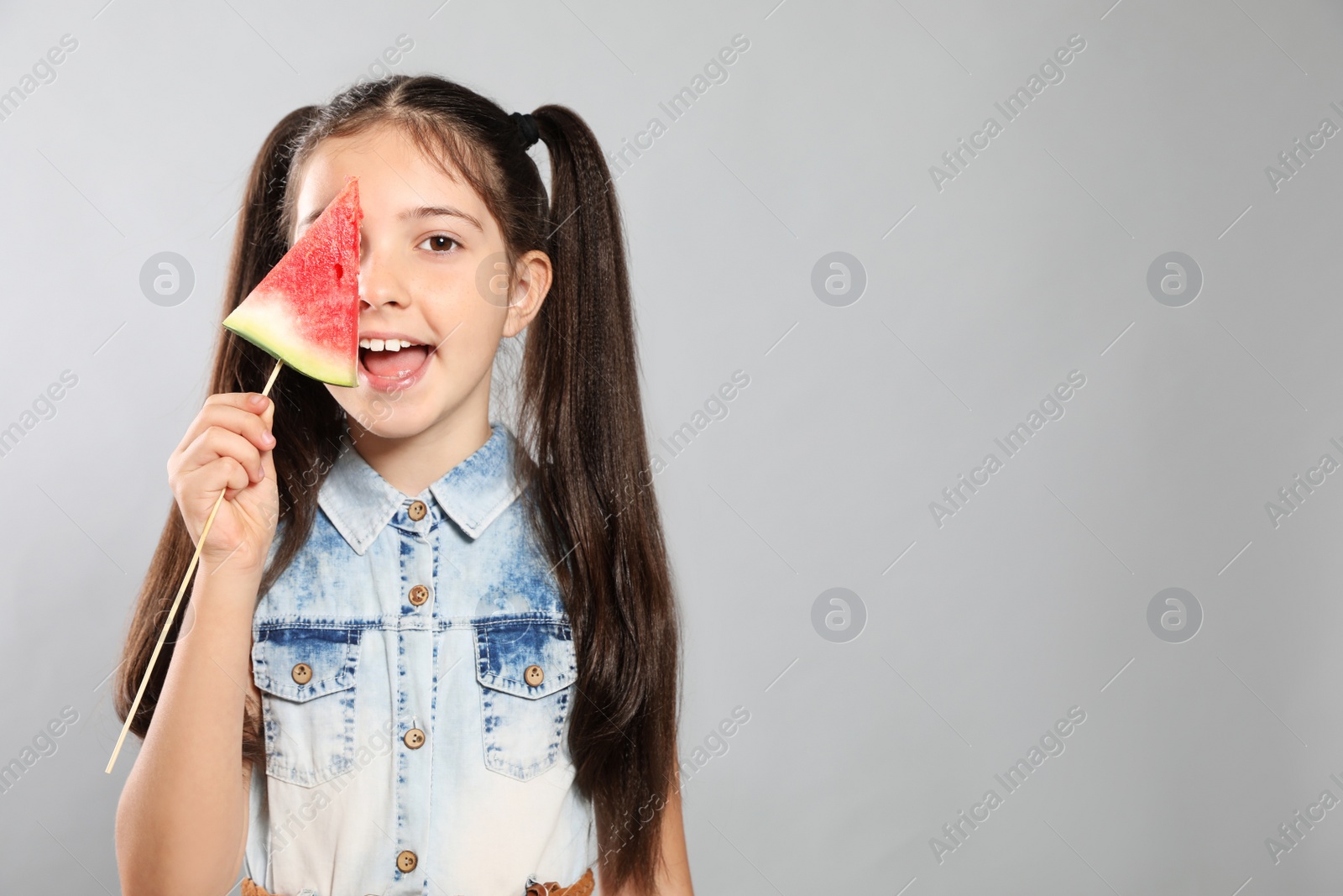 Photo of Cute little girl with watermelon on grey background. Space for text