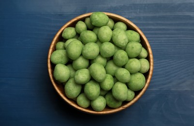 Photo of Tasty wasabi coated peanuts in bowl on blue wooden table, top view