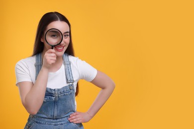 Happy young woman looking through magnifier glass on yellow background. Space for text