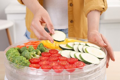Photo of Woman putting cut zucchini into fruit dehydrator machine in kitchen, closeup