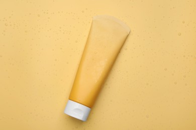 Wet tube of face cleansing product on pale orange background, top view