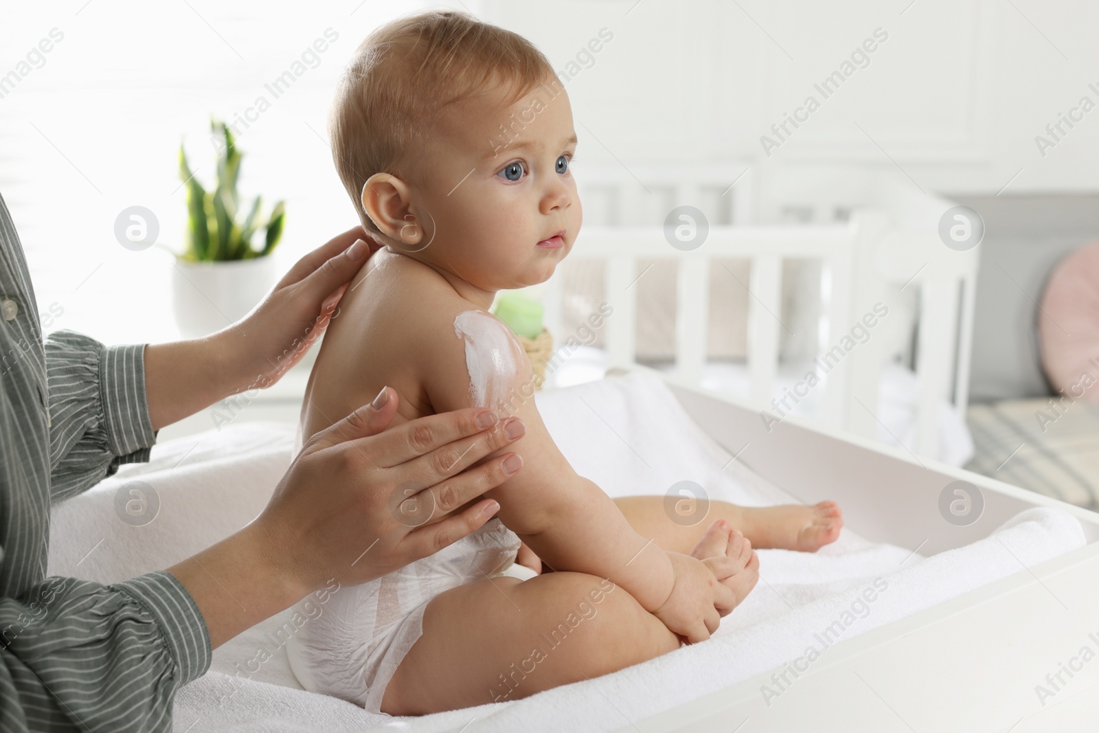 Photo of Mother applying body cream on her little baby at home, closeup