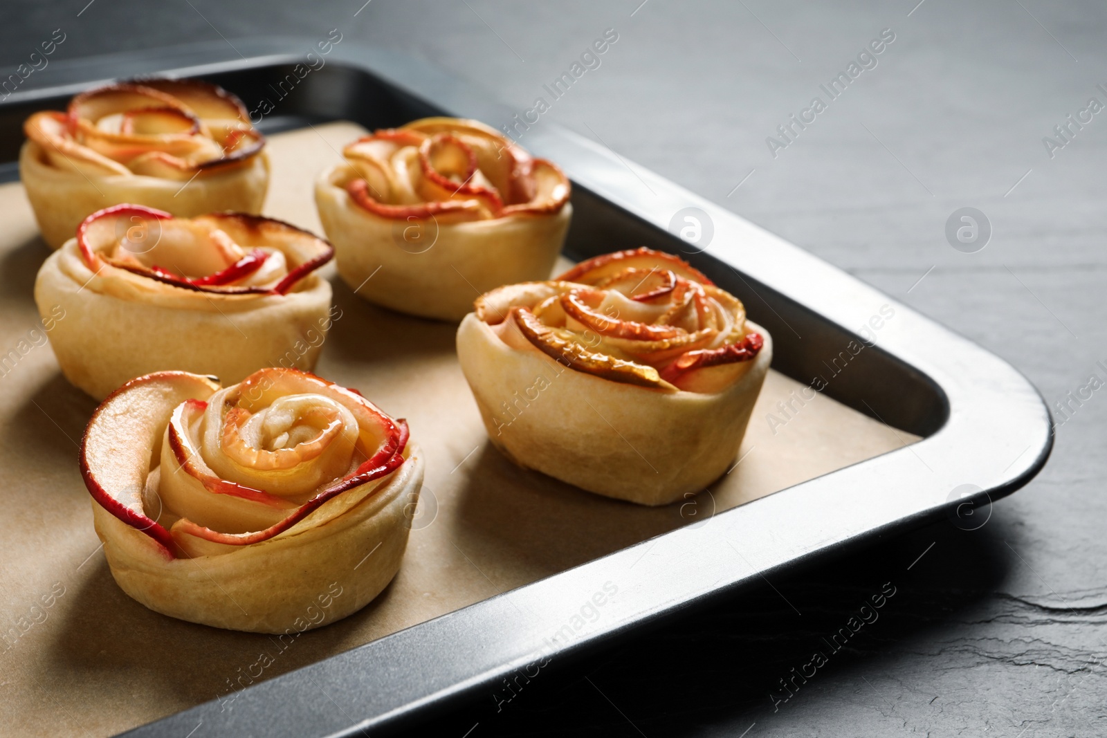 Photo of Tray with freshly baked apple roses on black table, closeup. Beautiful dessert
