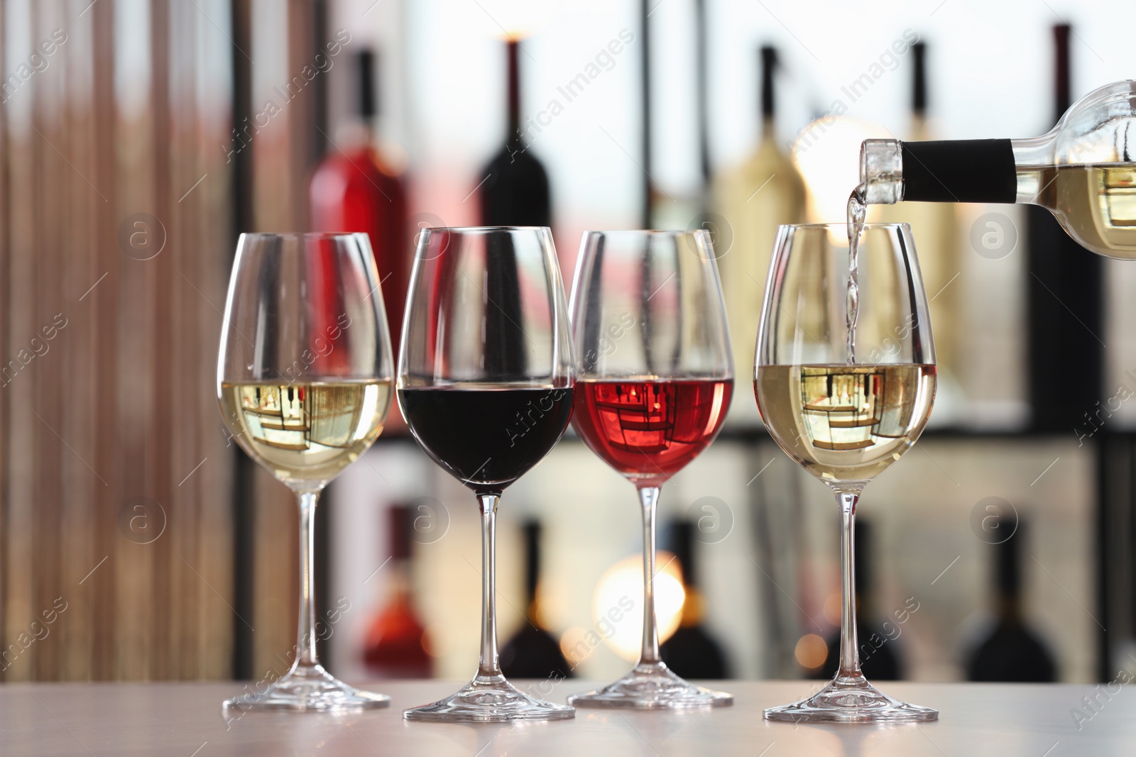 Photo of Pouring white wine from bottle into glass on table indoors