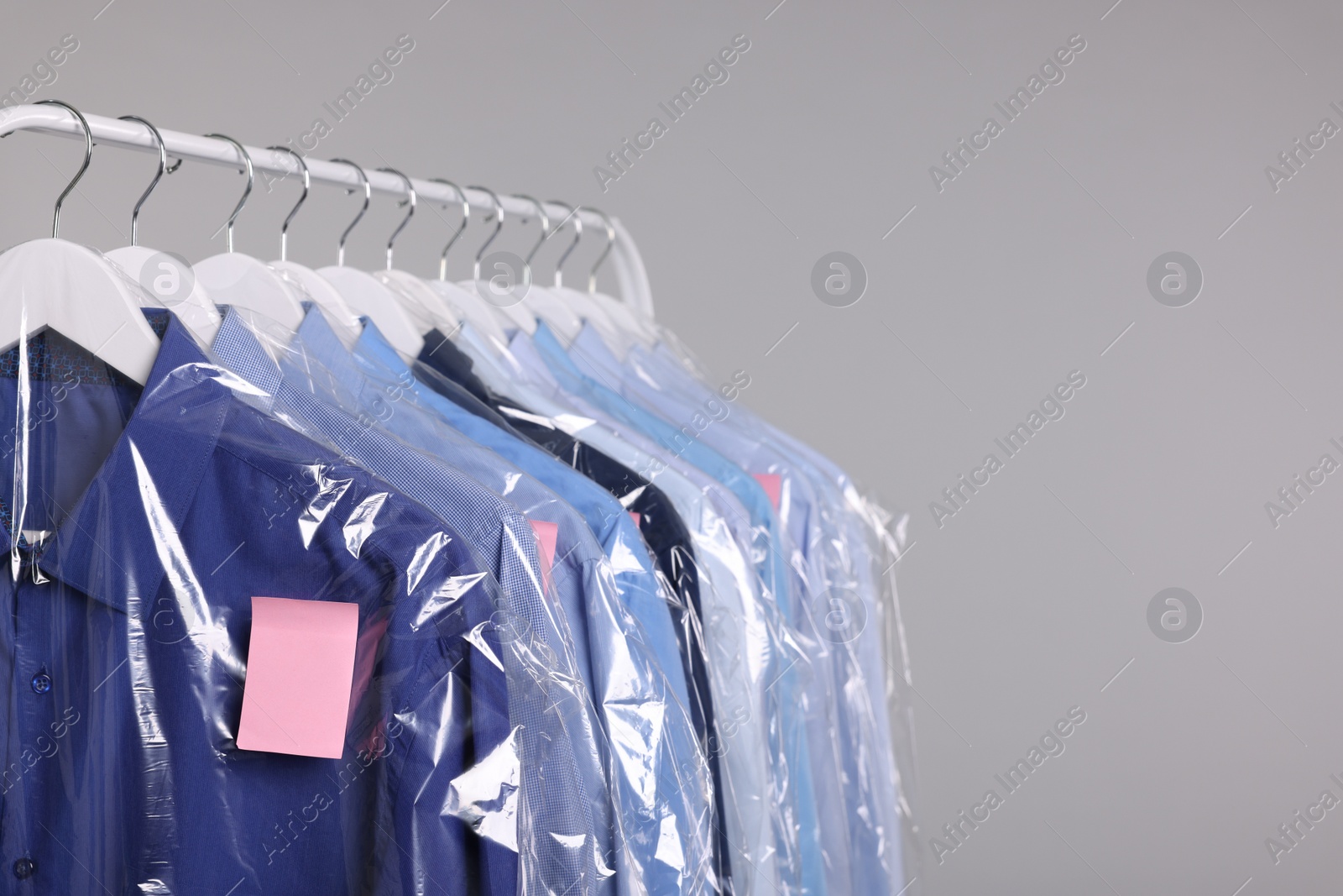 Photo of Dry-cleaning service. Many different clothes in plastic bags hanging on rack against grey background, space for text