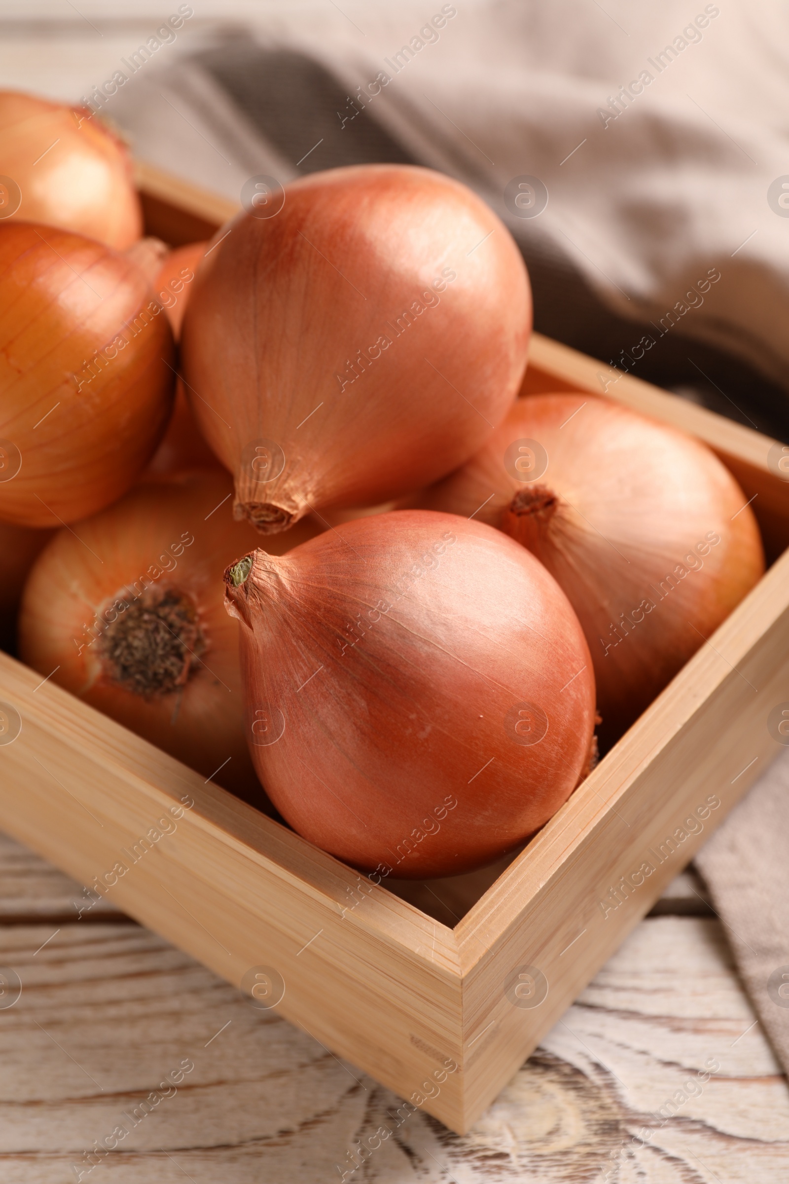 Photo of Crate with ripe onions on white wooden table, closeup