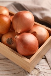 Photo of Crate with ripe onions on white wooden table, closeup