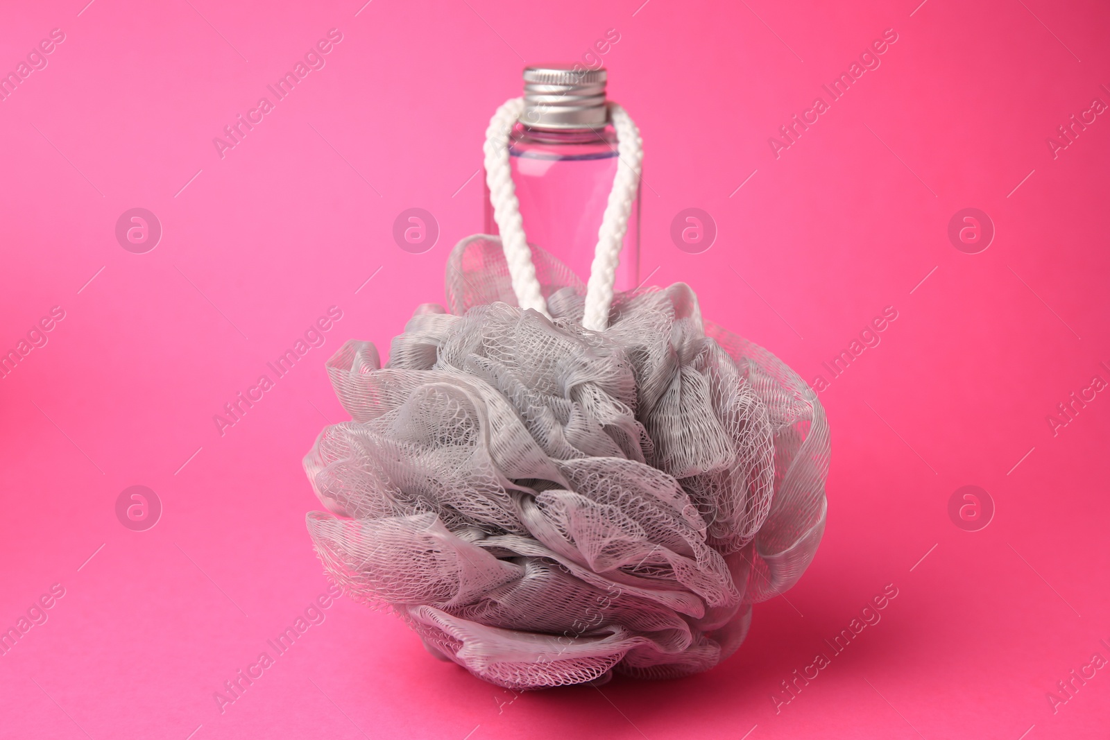 Photo of Grey shower puff and bottle of cosmetic product on pink background