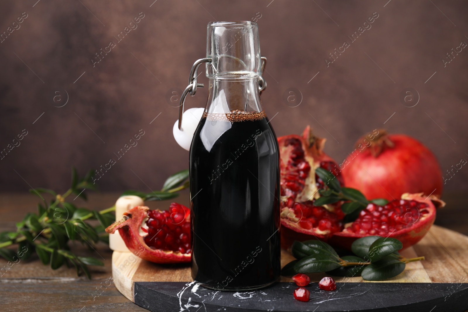 Photo of Tasty pomegranate sauce in bottle, fruits and branches on wooden table, closeup