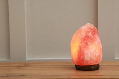 Photo of Himalayan salt lamp on wooden table near white wall indoors, space for text