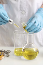 Photo of Scientist developing cosmetic oil at white table, closeup