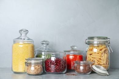 Glass jars with different types of groats on grey marble table