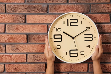 Woman touching clock on brick wall, space for text. Time management