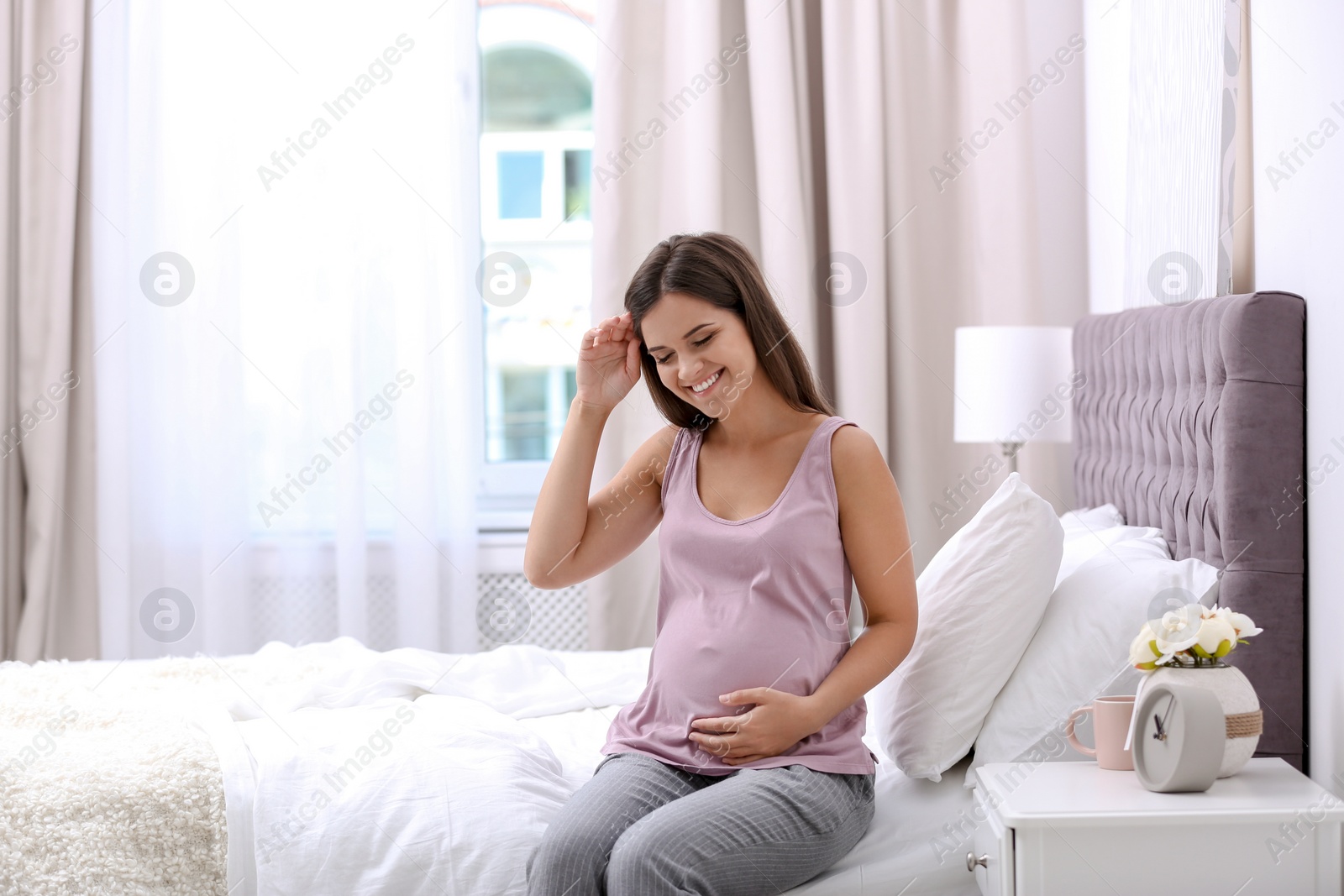 Photo of Happy pregnant woman sitting on bed at home