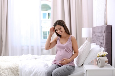 Photo of Happy pregnant woman sitting on bed at home