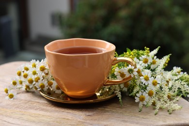 Photo of Cup of delicious chamomile tea and fresh flowers outdoors