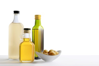 Photo of Bottles of different cooking oils and olives on white background, space for text